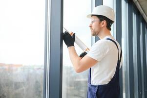 Workman in overalls installing or adjusting plastic windows in the living room at home photo