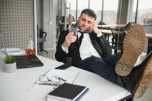 Old male employee drinking alcohol at workplace photo