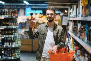 un hombre toma alcohólico bebidas desde el supermercado estante. compras para alcohol en el Tienda foto