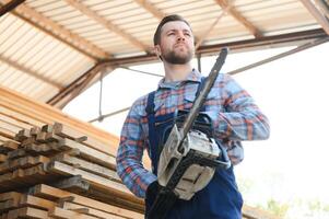 Carpenter with a saw in his hands stands on a background of cut wooden boards. photo