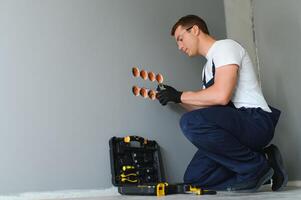 Electrician with screwdriver repairing power socket in room photo