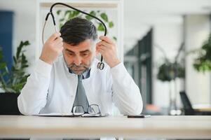 Mature doctor man at the clinic tired rubbing nose and eyes feeling fatigue and headache. stress and frustration concept. photo