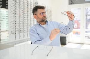 hermoso mayor hombre elegir los anteojos marco en óptico almacenar. foto