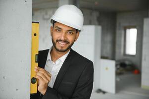 asiático ingeniero hermoso hombre o arquitecto con blanco la seguridad casco en construcción sitio. en pie a moderno edificio construcción. trabajador asiático hombre trabajando proyecto edificio foto