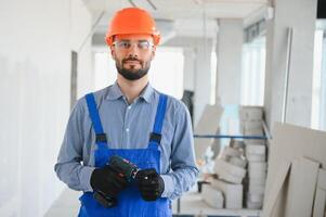 Portrait of positive, handsome young male builder in hard hat while working at construction site photo