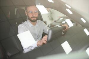 contento caucásico hombre en formal vestir consiguiendo dentro lujo moderno coche para pruebas interior antes de compra. concepto de concesión, de venta y compra foto