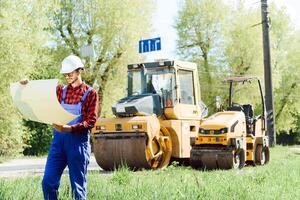 Smiling engineer with helmet standing in front of excavator on road construction site photo