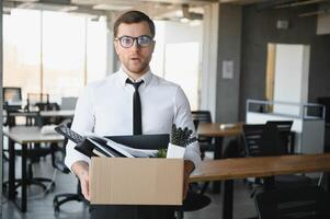 Sad Fired. Let Go Office Worker Packs His Belongings into Cardboard Box and Leaves Office. Workforce Reduction, Downsizing, Reorganization, Restructuring, Outsourcing. Mass Unemployment Market Crisis photo