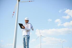 Engineer India man working at windmill farm Generating electricity clean energy. Wind turbine farm generator by alternative green energy. Asian engineer checking control electric power photo