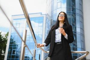 retrato de exitoso negocio mujer yendo a trabajo con café caminando cerca oficina edificio en ciudad calle. foto