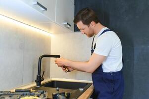 Professional plumber fixing water tap in kitchen photo