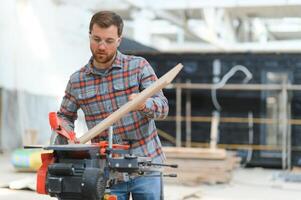 A carpenter works on woodworking the machine tool. Man collects furniture boxes. Saws furniture details with a circular saw. Process of sawing parts in parts. Against the background of the workshop. photo