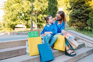 Young mother and her daughter doing shopping together. woman with girl child after shopping in street. woman with daughter with shopping bags outdoors. Woman and her daughter after shopping. photo