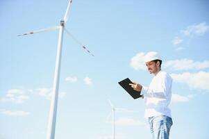 Engineer India man working at windmill farm Generating electricity clean energy. Wind turbine farm generator by alternative green energy. Asian engineer checking control electric power photo