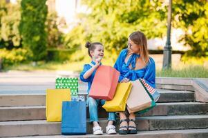 venta, consumismo y personas concepto - contento joven mujer su hija con compras pantalones caminando ciudad calle foto