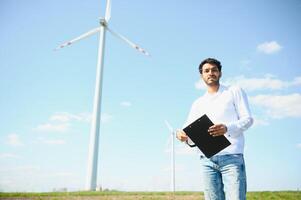 Engineer India man working at windmill farm Generating electricity clean energy. Wind turbine farm generator by alternative green energy. Asian engineer checking control electric power photo