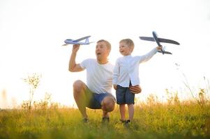 Cute little boy and his handsome young dad are smiling while playing with a toy airplane in the park. photo