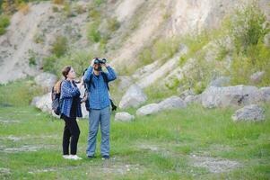 Couple of Young Happy Travelers Hiking with Backpacks on the Beautiful Rocky Trail at Warm Sunny Evening. Family Travel and Adventure Concept. photo