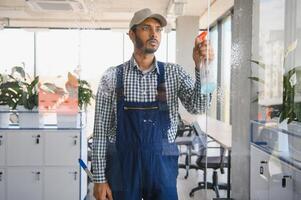 Indian Male professional cleaning service worker cleans the windows and shop windows of a store with special equipment photo