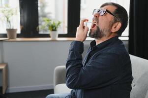 Sick senior man using throat spray at home photo