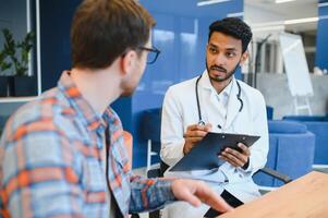 medicine, healthcare and people concept - indian doctor young male patient meeting at hospital photo