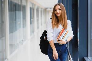 Portrait of a pretty female student with books and a backpack in the university hallway photo