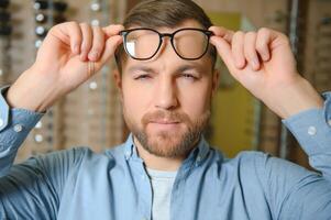 joven hombre elegir gafas a óptico tienda foto