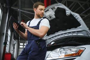 Automobile computer diagnosis. Car mechanic repairer looks for engine failure on diagnostics equipment in vehicle service workshop photo