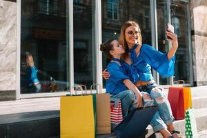 Young mother and her daughter doing shopping together. woman with girl child after shopping in street. woman with daughter with shopping bags outdoors. Woman and her daughter after shopping photo