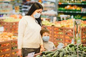 joven mujer y su niño vistiendo protector cara mascaras tienda un comida a un supermercado durante el coronavirus epidemia o gripe brote. foto