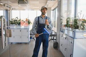 Indian Male professional cleaning service worker cleans the windows and shop windows of a store with special equipment photo