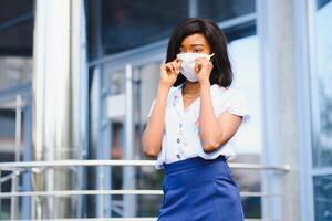 africano americano mujer de negocios vistiendo protector máscara en su cara en el ciudad. el concepto de visitando trabajo durante un pandemia foto