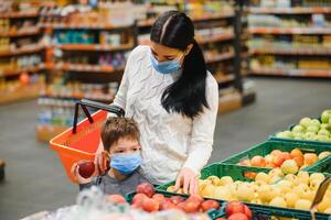 Mother and her son wearing protective face mask shop at a supermarket during the coronavirus epidemic. photo