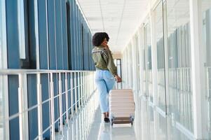 Young african american female passanger in casual clothes is in airport with baggage. photo