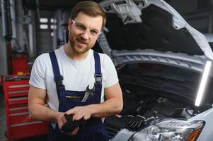 Portrait of a young beautiful car mechanic in a car workshop, in the background of service. Concept repair of machines, fault diagnosis, repair specialist, technical maintenance and on-board computer photo