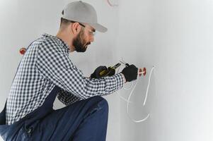 profesional electricista trabajando en un hogar eléctrico sistema, él es instalando un pared enchufe foto