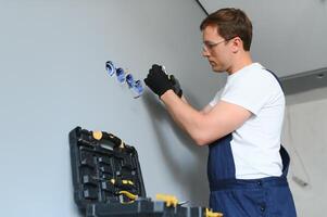 Electrician Builder at work, installation of sockets and switches. Professional in overalls with an electrician's tool. Against the background of the repair site. photo