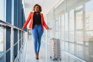 Full length side portrait of young black woman walking with suitcase in airport photo