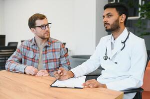 medicine, healthcare and people concept - indian doctor giving prescription to male patient at clinic photo