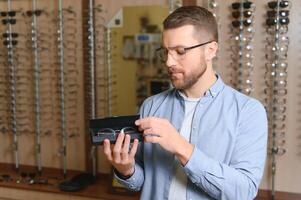 cuidado de la salud, vista y visión concepto. contento hombre elegir lentes a óptica almacenar, selectivo atención foto