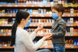 Mother applies sanitizer for cleaning son's hands in public crowded place. Shopping mall photo