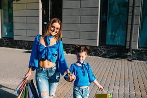 Young mother and her daughter doing shopping together. woman with girl child after shopping in street. woman with daughter with shopping bags outdoors. Woman and her daughter after shopping photo