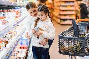 familia en el supermercado. hermosa joven mamá y su pequeño hija sonriente y comprando alimento. el concepto de sano comiendo. cosecha foto