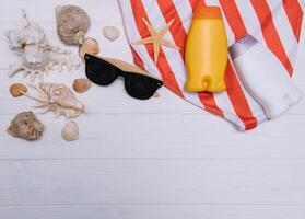 Beach accessories. Towel, flip-flops, starfish, boat and sunglasses on wooden background. Top view with copy space. Sunny toned photo