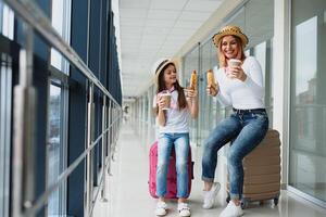 familia a aeropuerto antes de vuelo. madre y niño esperando a tablero a salida portón de moderno internacional Terminal. de viaje y volador con niños. mamá con bebé a embarque avión. foto