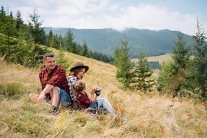 Family of three people rest in the mountains. They sat down to rest, drink water after a hard climb to the mountain. They are tired but happy photo