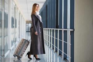 Portrait of successful business woman traveling with case at airport. Beautiful stylish female travel with luggage. photo