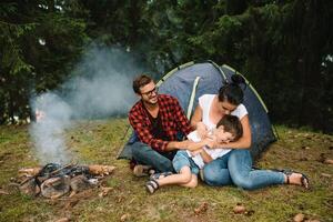 familia cerca el fuego en el bosque. padre con niño en un tienda antecedentes. nacional parque. caminata con niños. activo verano Días festivos foto