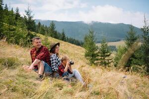 Family of three people rest in the mountains. They sat down to rest, drink water after a hard climb to the mountain. They are tired but happy. photo