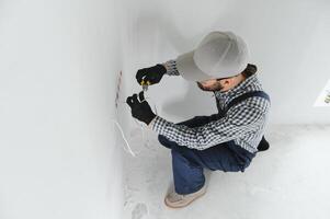 Professional electrician working on a home electrical system, he is installing a wall socket photo